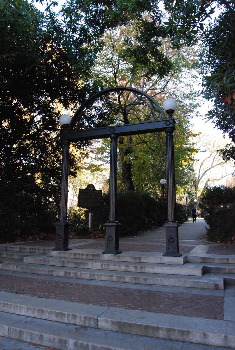 The black iron Arch at the top of brick steps, shaded by trees.