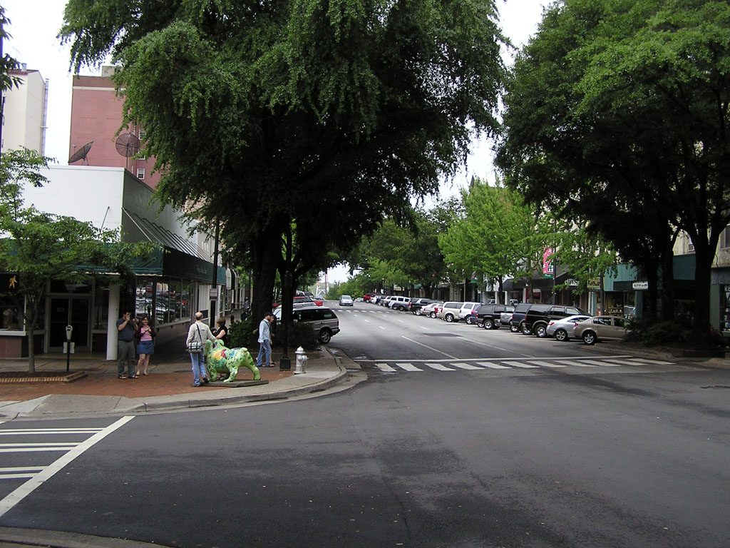 A tree-lined corner of College Avenue and Clayton Street in downtown Athens, with shops and a few pedestrians.