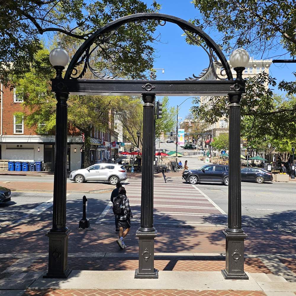 The Arch seen from the campus side, with a person walking through and downtown street traffic beyond.