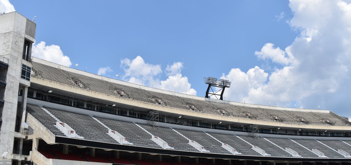 The empty north stands of Sanford Stadium under a blue sky with white clouds.