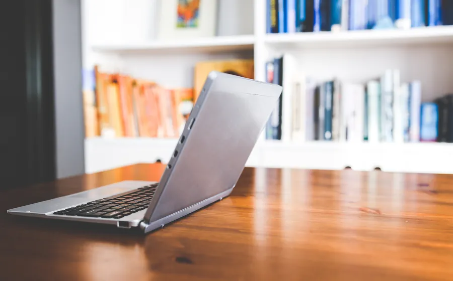 Laptop on a wooden desk in front of a bookshelf