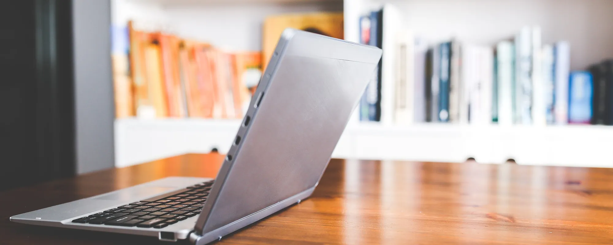 Laptop on a wooden desk in front of a bookshelf
