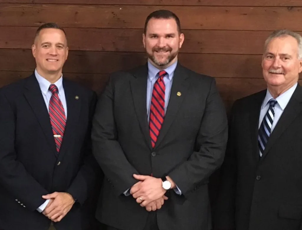 Three members of the Oglethorpe County Sheriff's Office command staff in suits, standing in front of a wood-panel wall